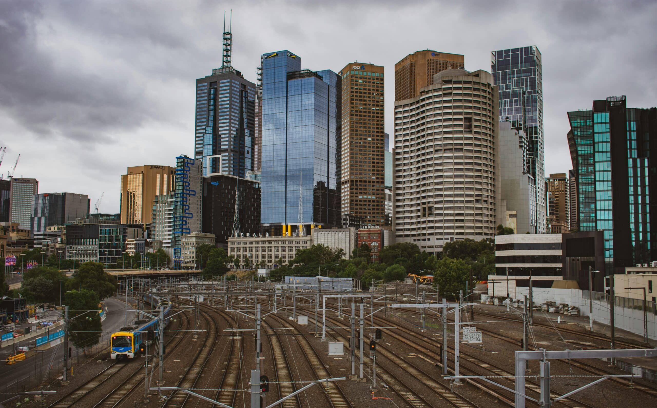 Dramatic urban skyline with train tracks leading into the city center under overcast skies.